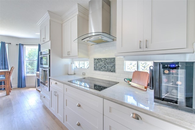 kitchen with black electric stovetop, decorative backsplash, stainless steel double oven, white cabinets, and wall chimney exhaust hood