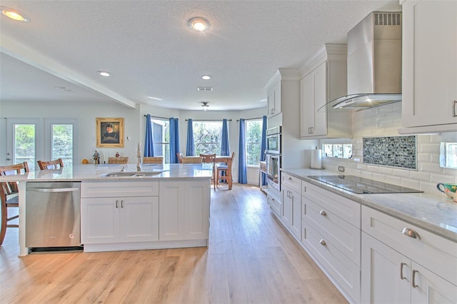 kitchen featuring a sink, stainless steel appliances, white cabinets, wall chimney exhaust hood, and light wood-type flooring