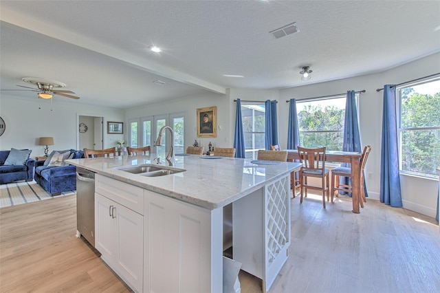 kitchen featuring a sink, open floor plan, light wood-style flooring, white cabinetry, and stainless steel dishwasher