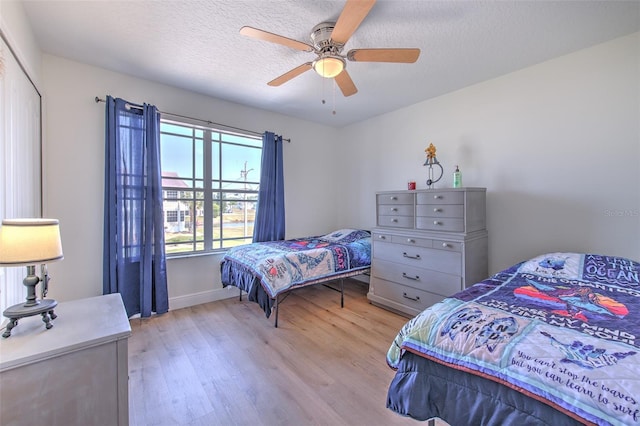 bedroom featuring baseboards, a textured ceiling, light wood-type flooring, and ceiling fan