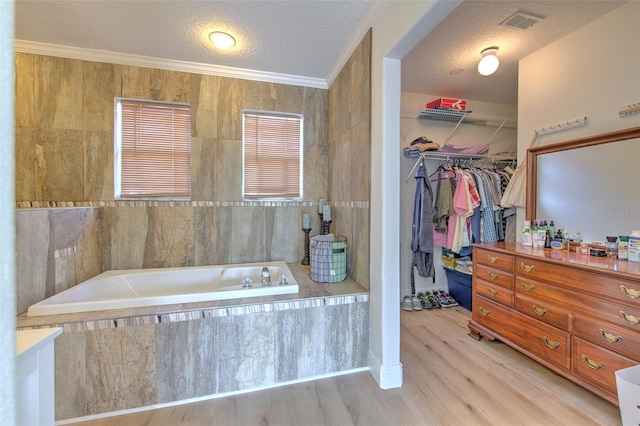 full bathroom featuring wood finished floors, visible vents, a textured ceiling, a walk in closet, and a bath