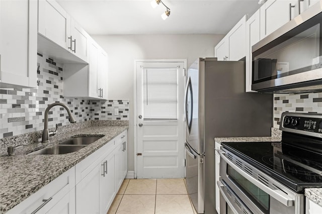 kitchen with light tile patterned floors, appliances with stainless steel finishes, white cabinets, and a sink