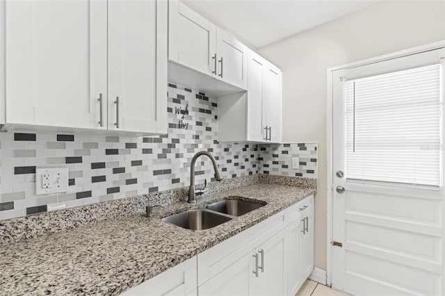 kitchen with light stone counters, backsplash, white cabinetry, a sink, and light tile patterned flooring