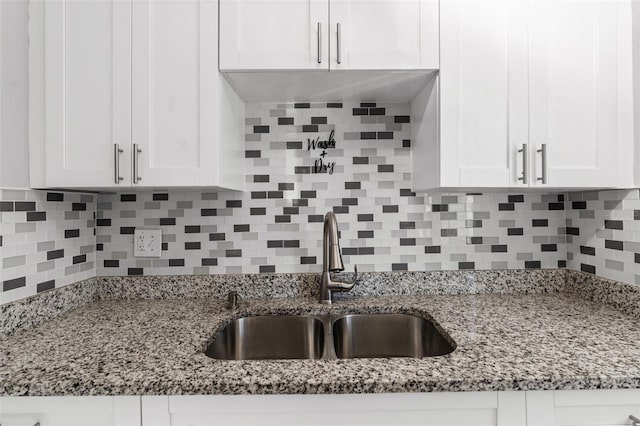 kitchen featuring light stone countertops, tasteful backsplash, white cabinets, and a sink