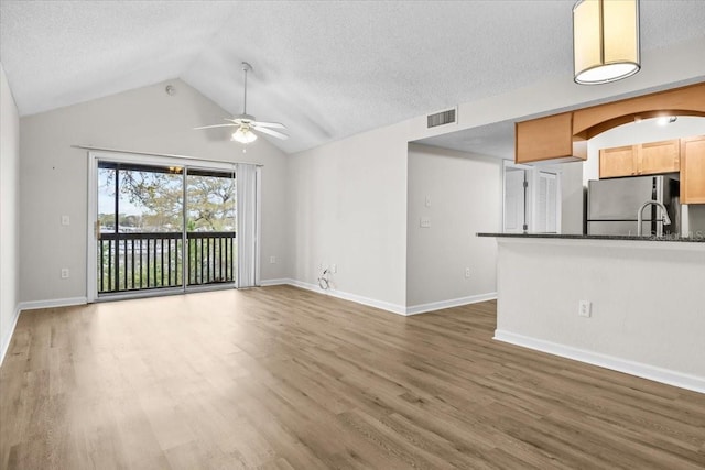 unfurnished living room with visible vents, vaulted ceiling, a textured ceiling, and wood finished floors