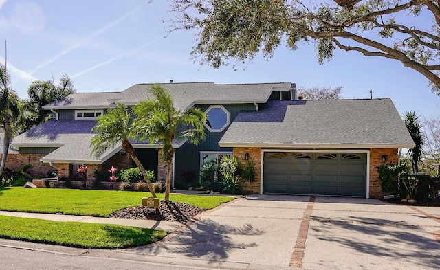 view of front facade with a front yard, driveway, an attached garage, a shingled roof, and brick siding