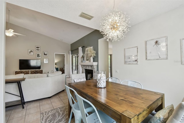 dining space featuring light tile patterned floors, visible vents, vaulted ceiling, a stone fireplace, and ceiling fan with notable chandelier