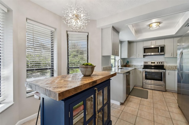 kitchen featuring a raised ceiling, wood counters, appliances with stainless steel finishes, a sink, and light tile patterned flooring