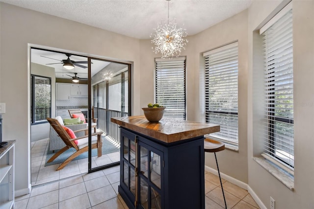 dining area featuring ceiling fan with notable chandelier, a textured ceiling, baseboards, and light tile patterned floors