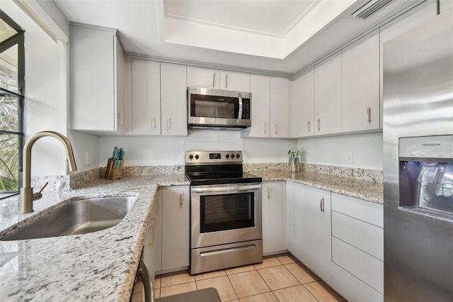 kitchen with light tile patterned floors, a raised ceiling, appliances with stainless steel finishes, white cabinets, and a sink