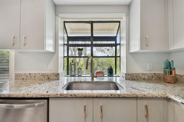 kitchen with light stone countertops, dishwasher, white cabinetry, and a sink