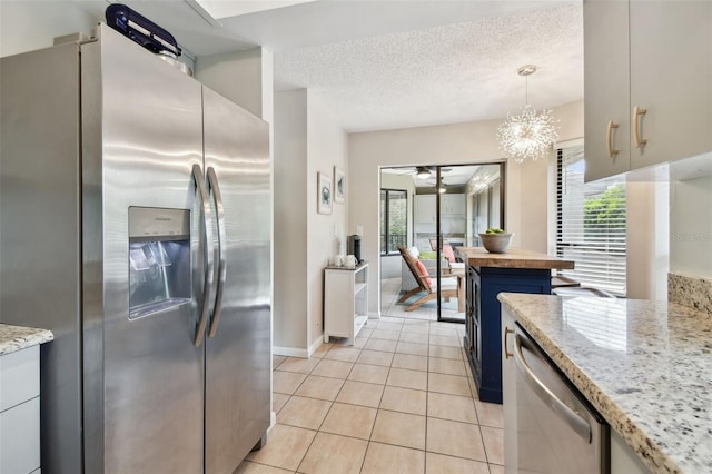 kitchen with a textured ceiling, appliances with stainless steel finishes, light tile patterned flooring, and a wealth of natural light