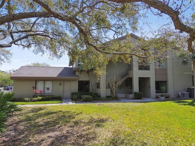 view of front of house featuring central AC unit, stairway, a front lawn, and stucco siding