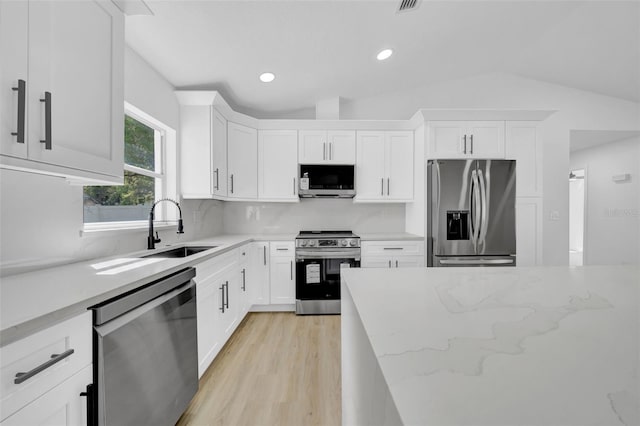 kitchen featuring light stone counters, decorative backsplash, stainless steel appliances, white cabinetry, and a sink