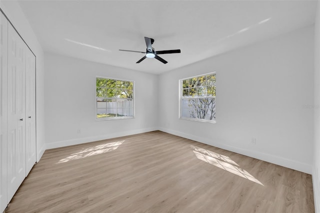 unfurnished bedroom with a closet, multiple windows, light wood-style floors, and baseboards