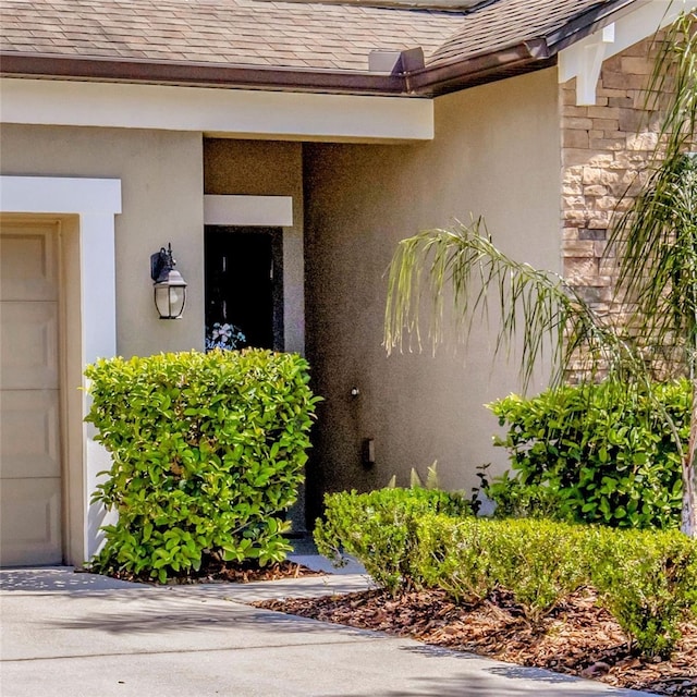 entrance to property with stucco siding, a shingled roof, and a garage