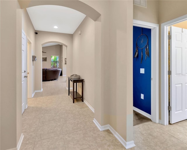 hallway with arched walkways, visible vents, baseboards, and light tile patterned floors