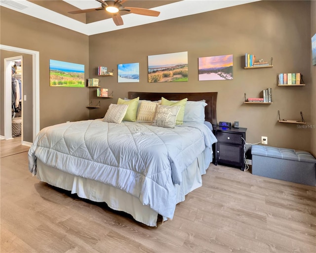 bedroom with a walk in closet, light wood-type flooring, and ceiling fan