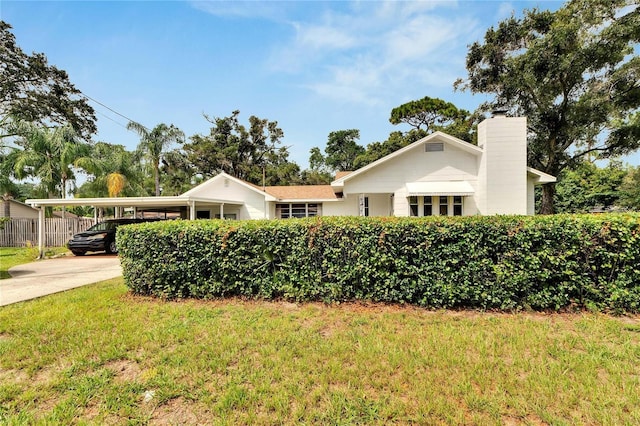 view of front of home featuring driveway, a chimney, fence, a carport, and a front yard