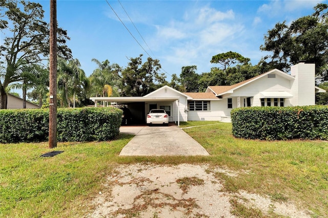 view of front of property with concrete driveway, a carport, a chimney, and a front yard