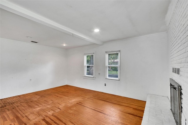 spare room featuring visible vents, hardwood / wood-style flooring, beamed ceiling, crown molding, and a brick fireplace