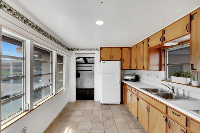 kitchen with tasteful backsplash, freestanding refrigerator, light countertops, and a sink