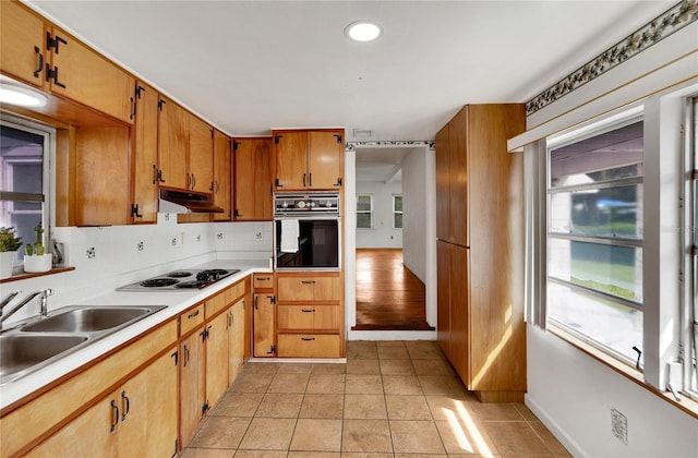 kitchen featuring tasteful backsplash, oven, black electric stovetop, under cabinet range hood, and a sink