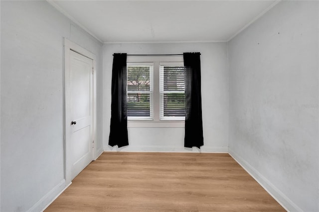 spare room with ornamental molding, baseboards, and light wood finished floors