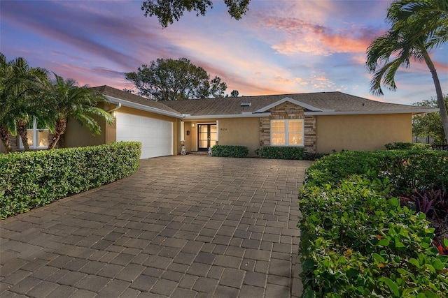 view of front facade featuring a garage, stone siding, decorative driveway, and stucco siding