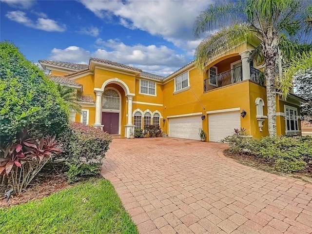 mediterranean / spanish-style house featuring a garage, a balcony, decorative driveway, and stucco siding