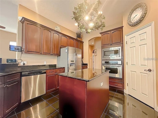 kitchen with arched walkways, dark stone counters, dark tile patterned flooring, appliances with stainless steel finishes, and a center island