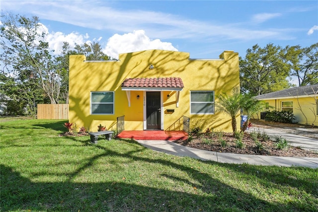 view of front of house with a front lawn, a tiled roof, fence, and stucco siding