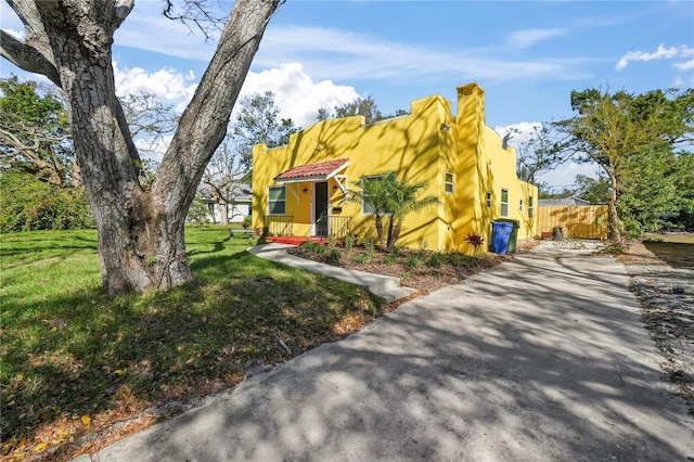 southwest-style home with stucco siding, a chimney, a front lawn, and fence