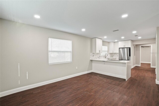 kitchen with tasteful backsplash, baseboards, dark wood finished floors, freestanding refrigerator, and a peninsula