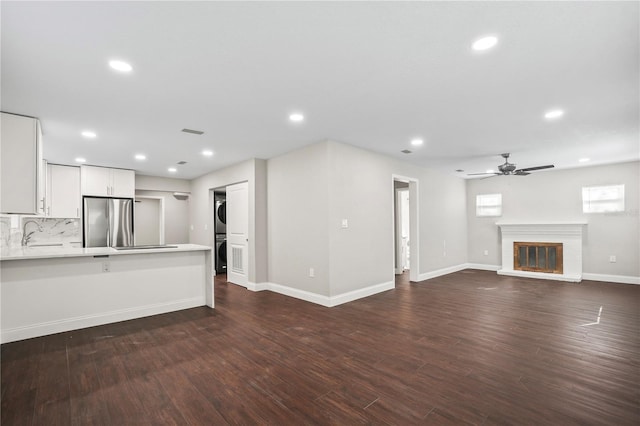 unfurnished living room with dark wood-style floors, stacked washer / dryer, a fireplace, and recessed lighting