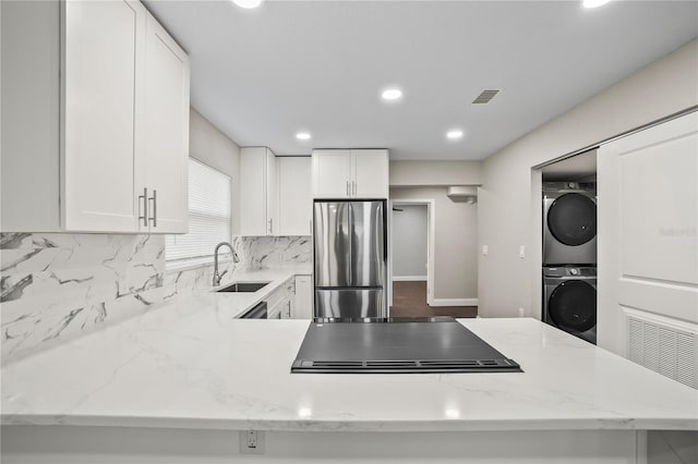 kitchen featuring tasteful backsplash, stacked washer / drying machine, freestanding refrigerator, a sink, and stovetop