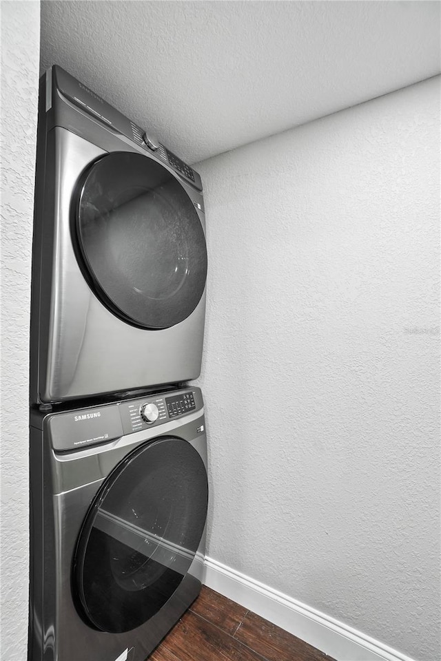 clothes washing area featuring a textured wall, laundry area, wood finished floors, baseboards, and stacked washing maching and dryer