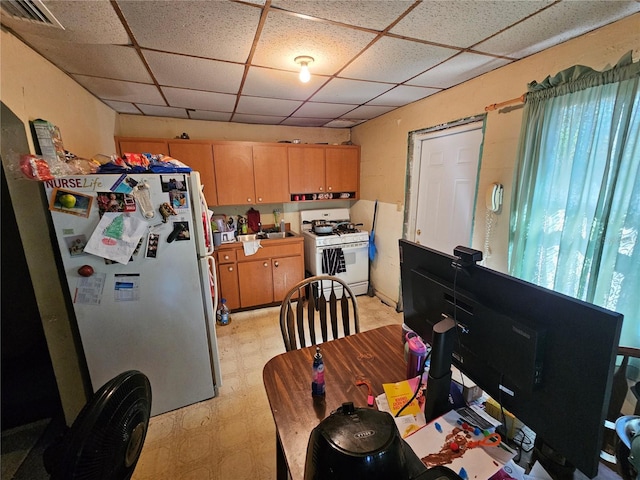 kitchen with light floors, visible vents, light brown cabinetry, white appliances, and a drop ceiling