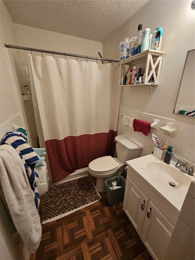 full bathroom with wainscoting, toilet, a textured ceiling, vanity, and tile walls