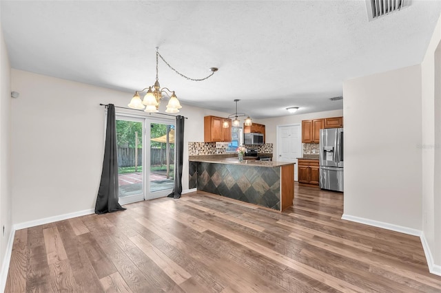 2412 Giddens Ave, Seffner, FL 33584 - kitchen with stainless steel appliances, a chandelier, brown cabinetry, decorative backsplash, and a peninsula