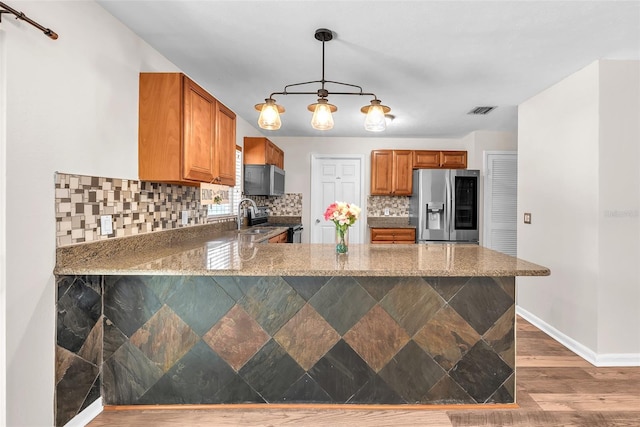2412 Giddens Ave, Seffner, FL 33584 - kitchen with appliances with stainless steel finishes, tasteful backsplash, brown cabinetry, light stone counters, and a peninsula