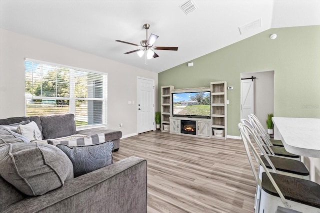 living area with visible vents, a barn door, light wood-style floors, ceiling fan, and a lit fireplace