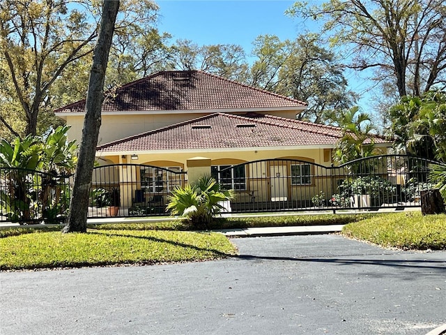 mediterranean / spanish house featuring a fenced front yard, a gate, a tiled roof, and stucco siding