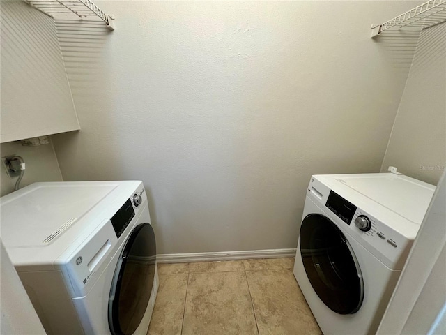 washroom featuring laundry area, baseboards, washing machine and clothes dryer, and light tile patterned flooring