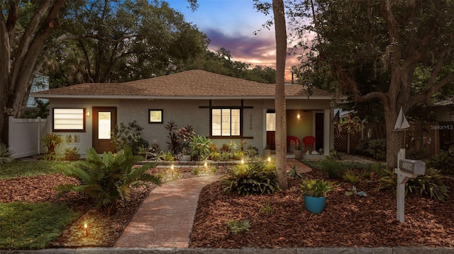 view of front of property featuring a shingled roof, fence, and stucco siding