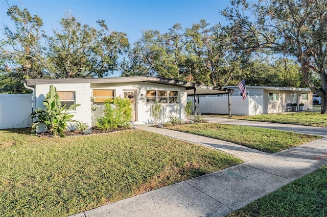 view of front of home featuring driveway, fence, a front lawn, a carport, and brick siding