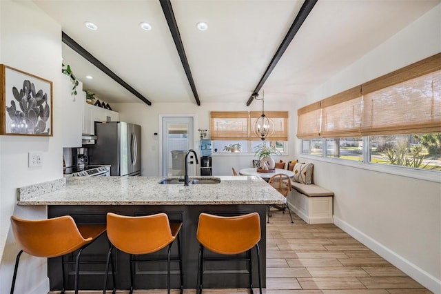 kitchen with a peninsula, a sink, white cabinetry, appliances with stainless steel finishes, and beam ceiling