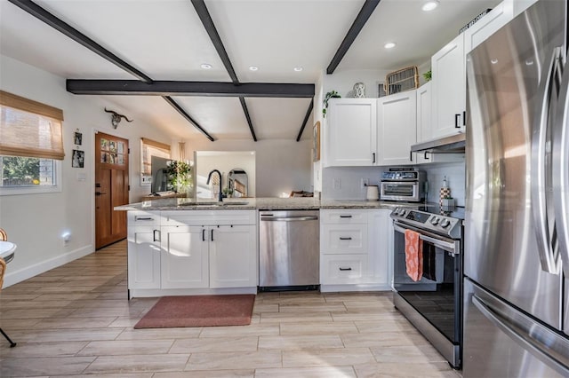 kitchen featuring appliances with stainless steel finishes, white cabinetry, a sink, light stone countertops, and a peninsula