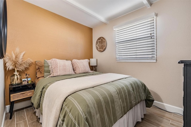 bedroom featuring baseboards, beamed ceiling, and wood finished floors