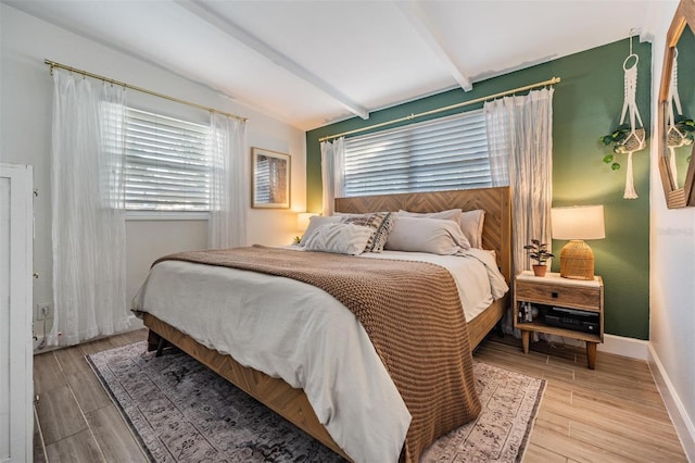 bedroom featuring lofted ceiling with beams, baseboards, and wood finished floors